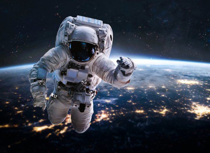 Astronaut floating above the earth with lights and countries visible on its surface.