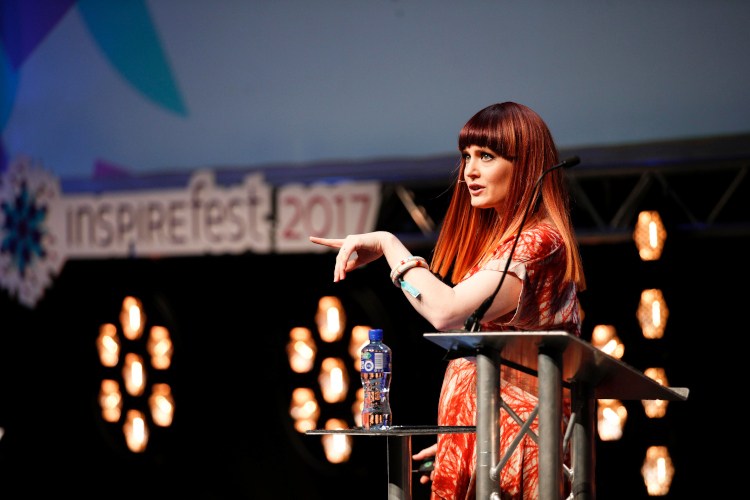 Ana Matronic stands at a podium on stage. Behind her is a sign that says Inspirefest 2017.