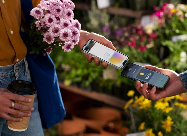 A customer at a florist pays for a bouquet by touching her iPhone to the seller’s iPhone.