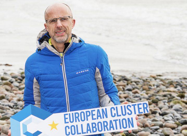 A man on a beach holds a sign that says 'European Cluster Collaboration'.