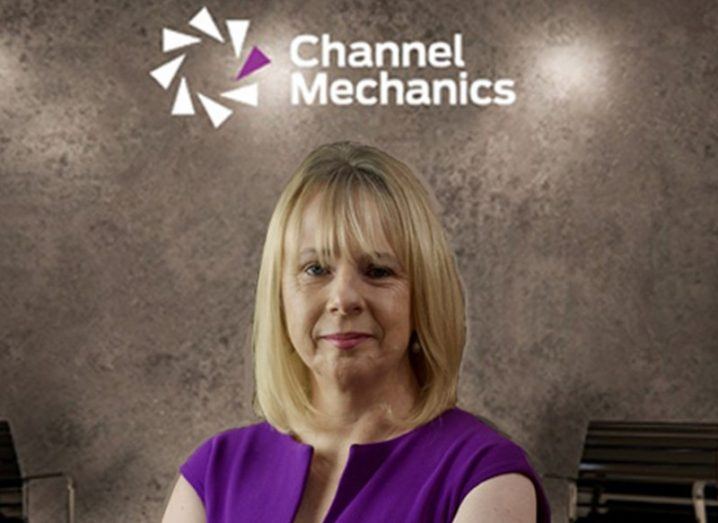 A blonde woman smiles at the camera. Behind her a wall that says Channel Mechanics.