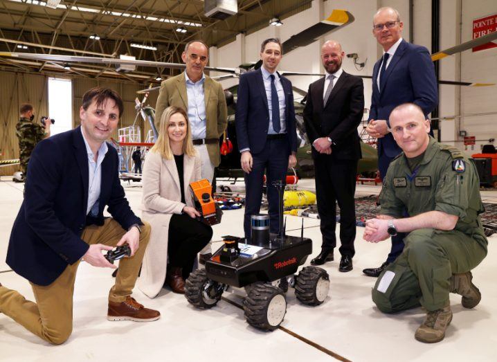 Ministers, academics and a member of the Defence Forces stand around a small remotely operated vehicle.