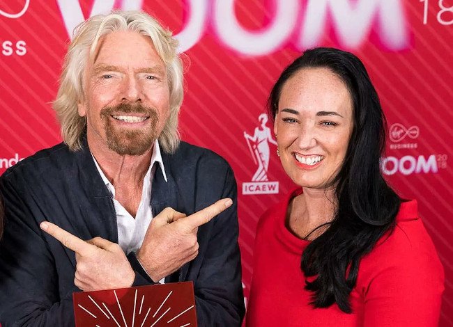 Richard Branson stands next to Tracey-Jane Cassidy against a red background that says Voom.