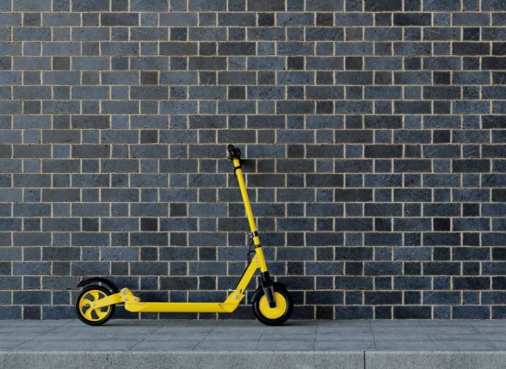 A yellow e-scooter parked in front of a grey brick wall.