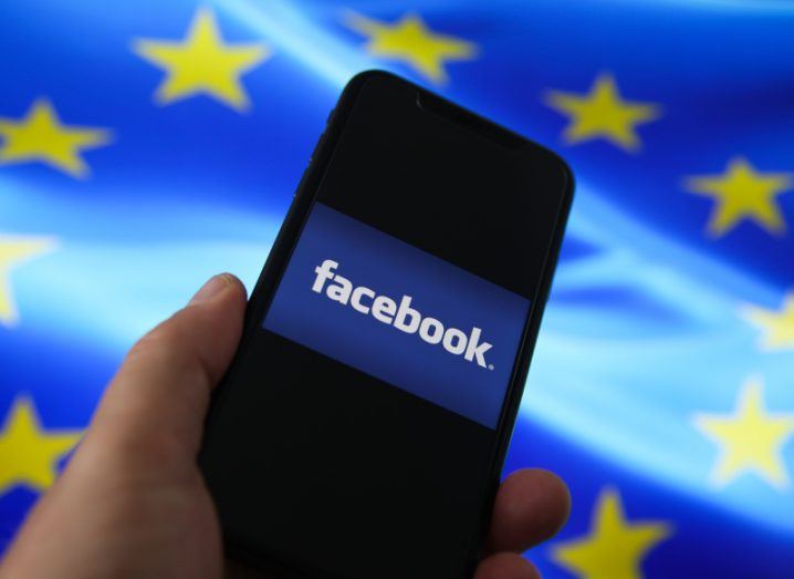 Facebook logo on a smartphone held in a hand. EU flag in the background.