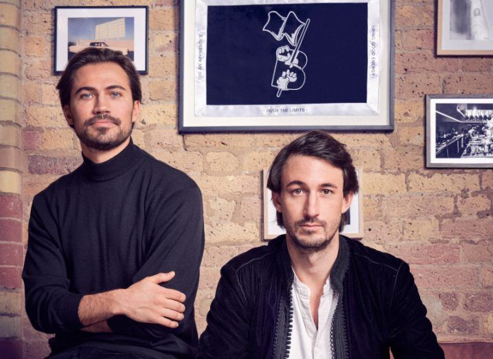 Backed co-founders Alex Brunicki and Andre de Haes, with a brick wall and paintings behind them.