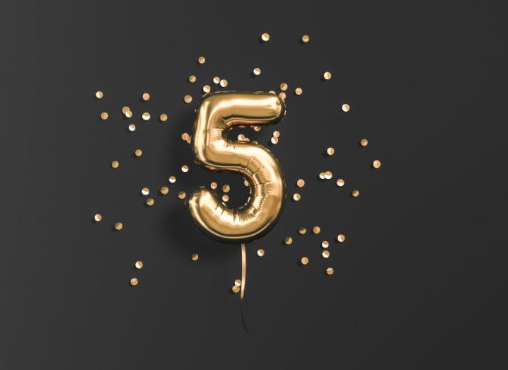 A golden balloon in the shape of the number five on a black background.