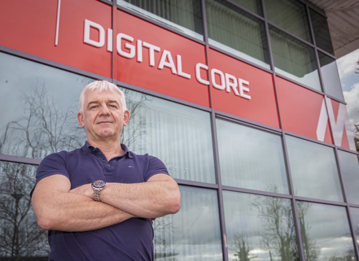 A man wearing a dark polo shirt stands outside a large glass building that says digital core on it, along with the Mercury Engineering logo.