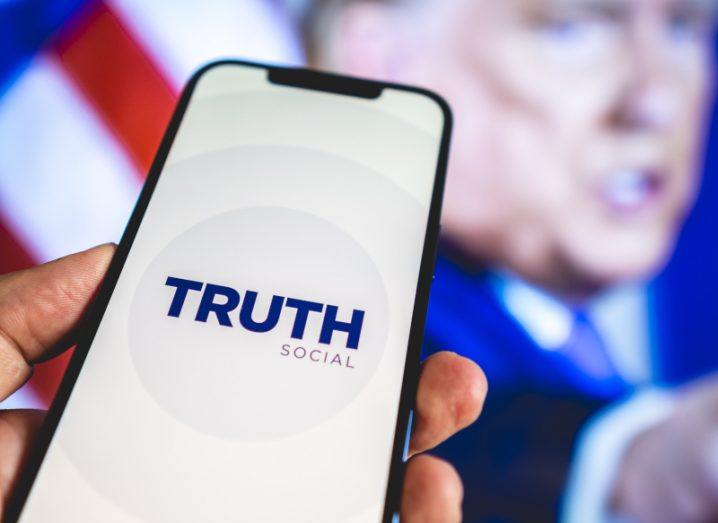 Truth Social app logo on a smartphone with image of Donald Trump in the background.
