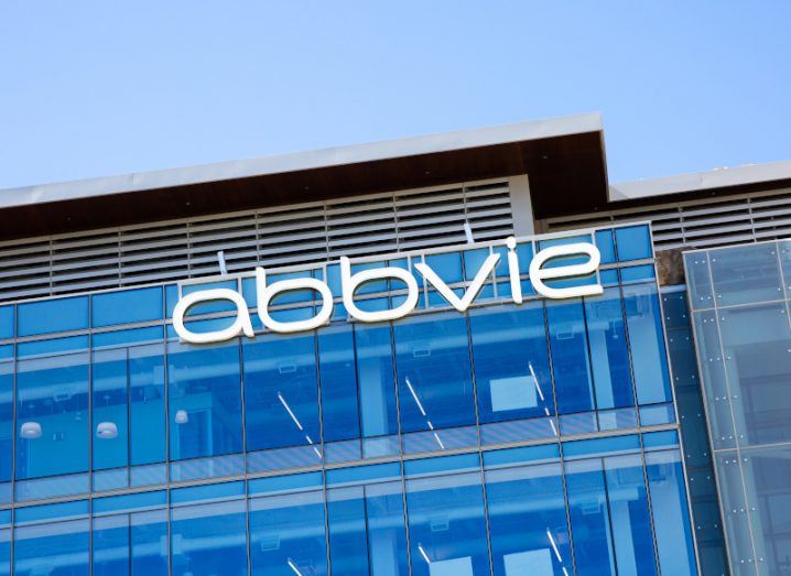 The AbbVie logo in white letters on top of a large glass building against a blue sky.