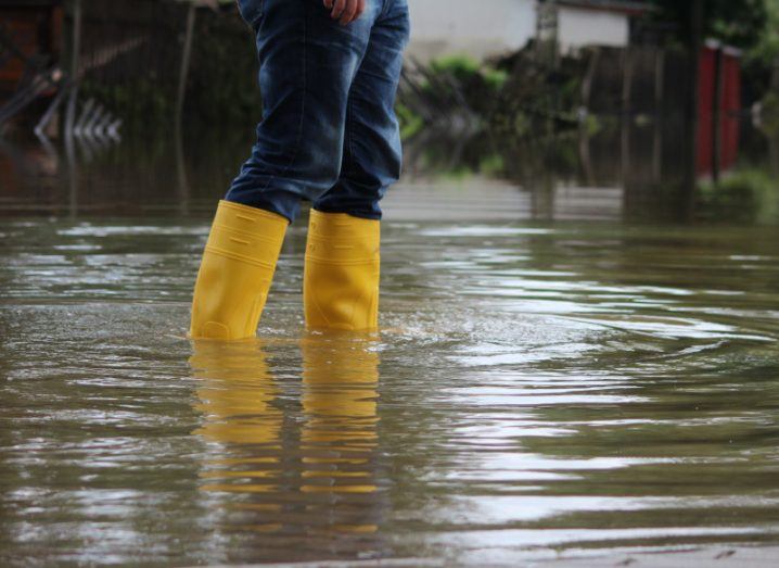 A person in wellington boots walks through a flooded street.
