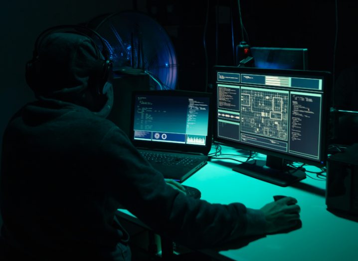 Hacker in front of two computer screens in a dark room.