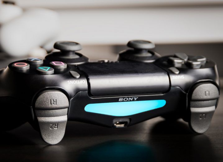 Sony PlayStation controller with the Sony logo visible above a blue light, with the controller resting on a table.