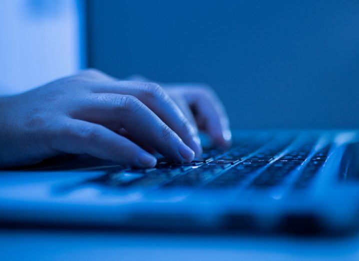 A pair of hands typing on a computer keyboard with blue lighting.
