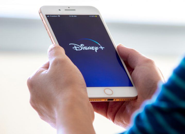A man holds an iPhone launching the Disney+ streaming app.