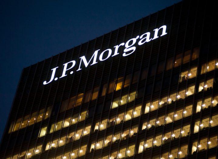 JP Morgan logo sign in white letters lit up over its office against the night sky.