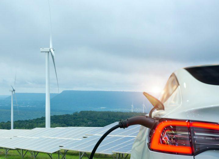 Electric car charging in front of windmills and solar panels in sustainable transport concept.