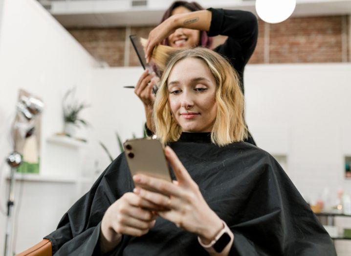 A woman receives a haircut in a salon while using her smartphone.