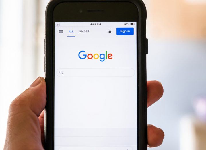 Mobile phone being held by someone with the Google logo and search icon on the screen.