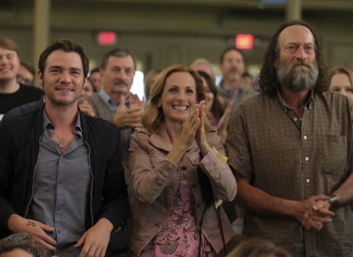 Actors Daniel Durant, Marlee Matlin and Troy Kotsur stand cheering in a crowd in a scene from CODA.