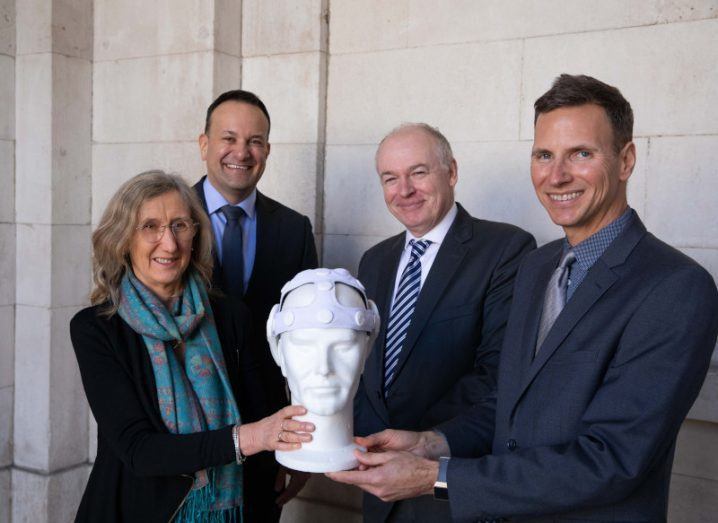Four people stand holding a model of a head with a brain monitoring device on it.