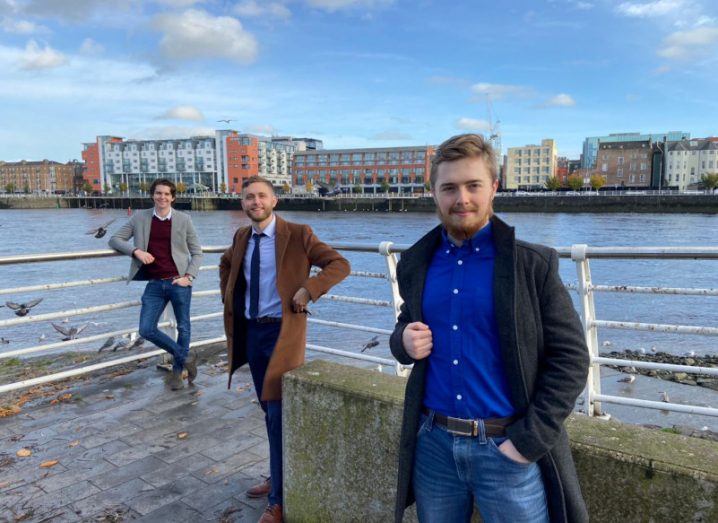 Three smartly dressed men stand on the banks of the River Shannon in Limerick city.