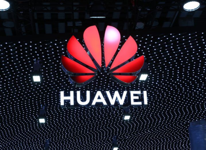 Huawei logo hanging under a ceiling with white lights above it.