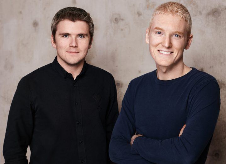 Stripe founders Patrick and John Collison stand side by side in dark shirts against a mottled grey background.