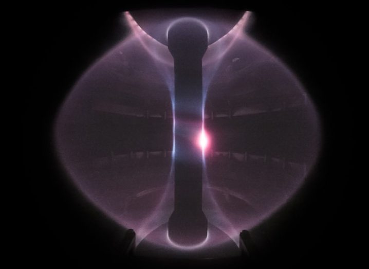 A view from inside the doughnut-shaped tokamak showing a purplish plasma cloud with a hot white centre.