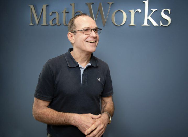 Richard Haxby stands smiling in front of a blue wall that says 'MathWorks' on it.