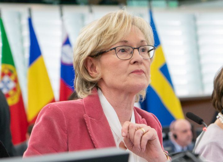 A woman seated in the European parliament stares into the distance with EU member-state flags in the background.