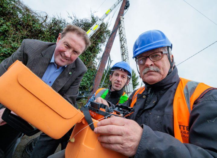 One man in a suit and two men in construction gear holding equipment and looking at the camera.