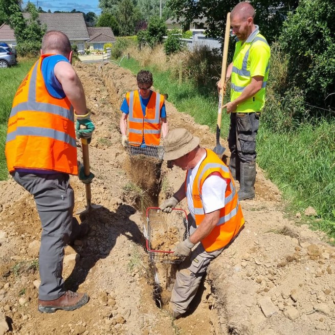 Four men wearing construction gear digging a hole in the ground to bury cables.