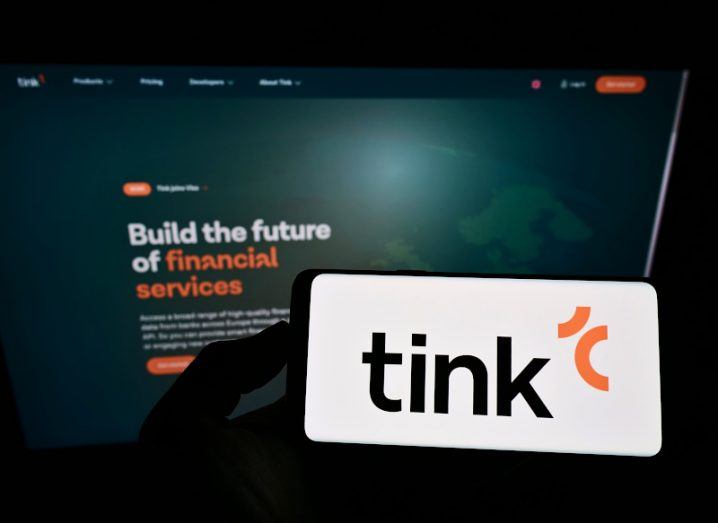 Silhouette of a hand holding a smartphone displaying the Tink logo. Text on a screen in the background reads "Build the future of financial services".