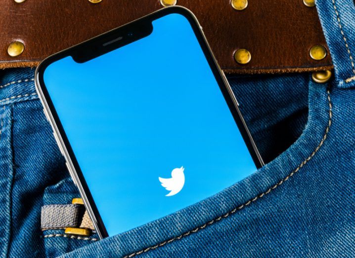 Twitter logo on a smartphone screen partially inside the front pocket of a pair of jeans.