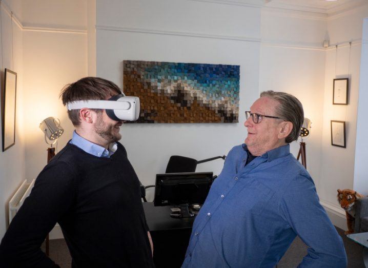 A man wearing a VR headset looks at another older man staring back at him.