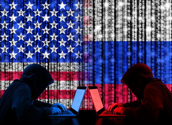Illustration of the silhouettes of two hackers with laptops facing each other with the US and Russian flag behind each.