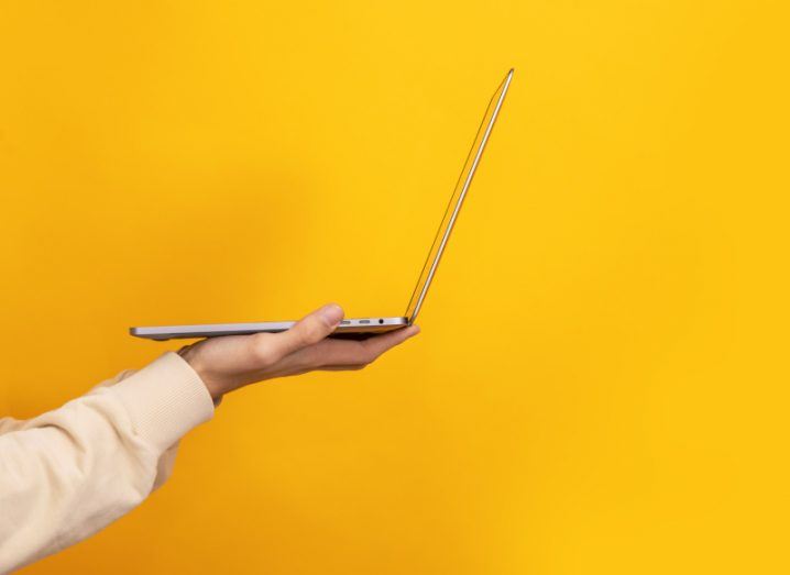 A person's palm holding up a laptop in a yellow background.
