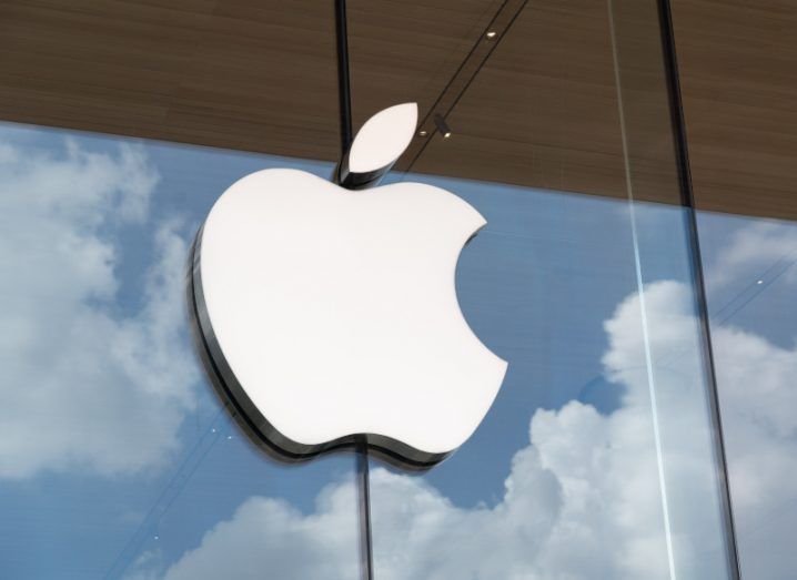 Apple logo on a glass window reflecting clouds.