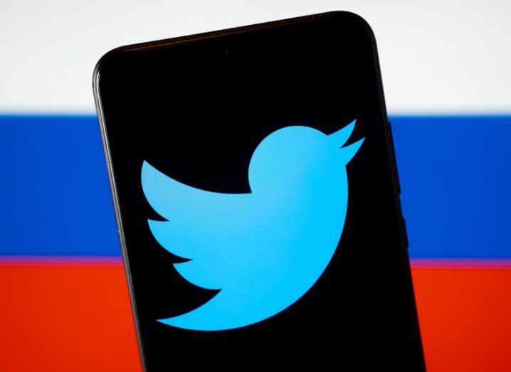 Twitter logo on a smartphone screen with Russian flag in the background.