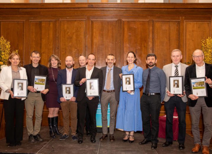 A line of 10 people standing on stage smiling at the camera. They represent some Trinity start-ups and some are holding framed certificates.