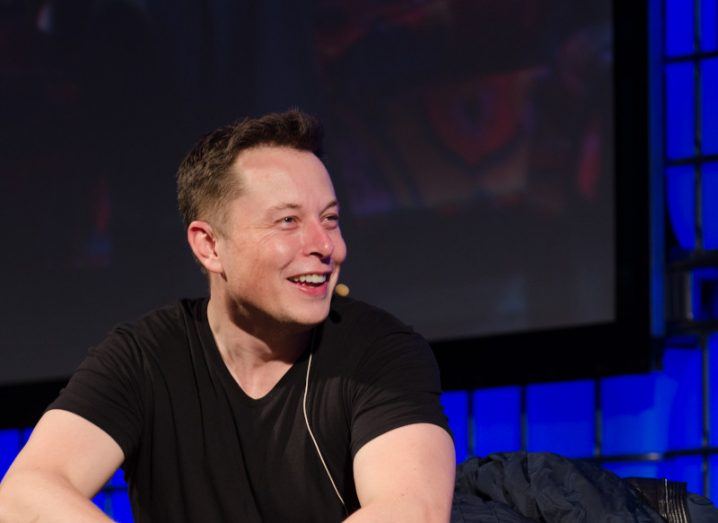 Elon Musk sits on a stage at a conference event.
