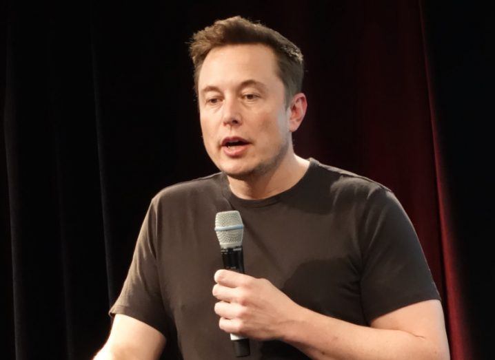 Elon Musk holding a microphone at a shareholder meeting.