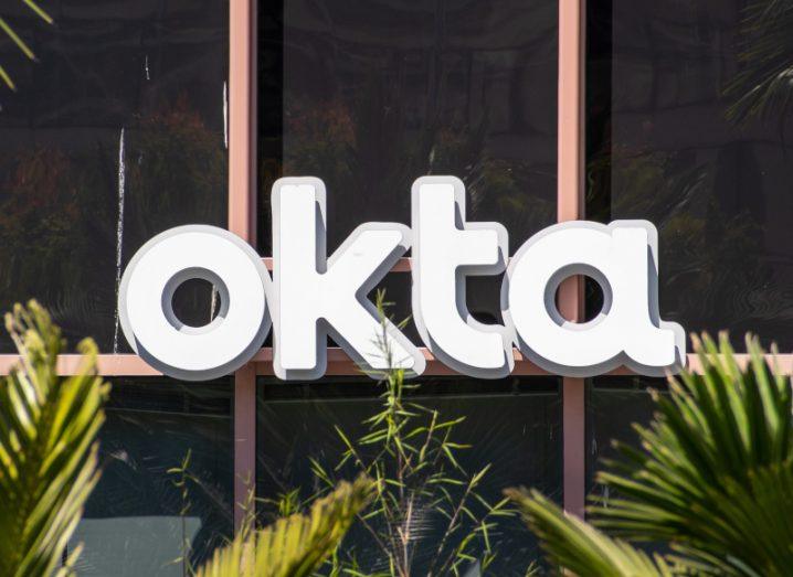Okta logo in front of a building with plants in front of it.