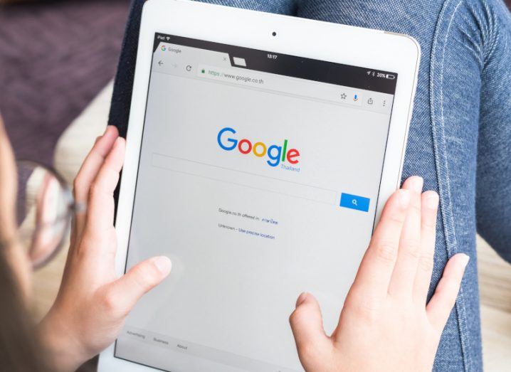Google logo above its search function, on a tablet screen being held by a person.
