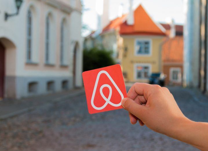 A person’s hand is holding up a card with the Airbnb logo on it against a cityscape of Minsk in Belarus.