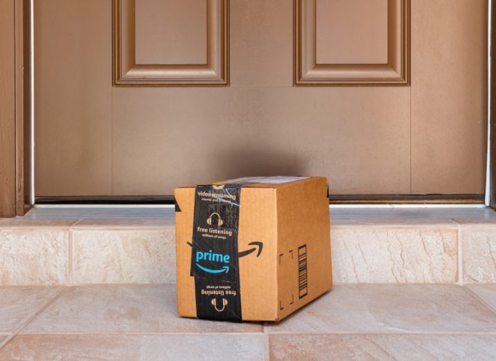 An Amazon Prime branded cardboard box sits on a doorstep outside a brown painted door.