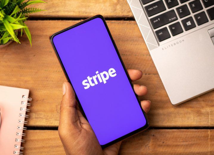 Stripe logo on a mobile phone being held by a person with a wooden table as the background.