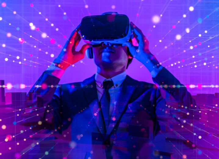 Business person wearing a suit and a metaverse headset looking into the distance against a purple background.