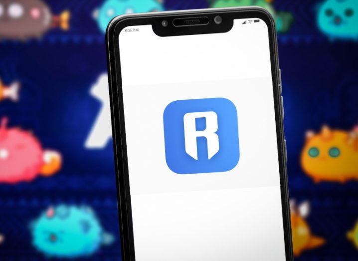 Ronin logo on a mobile phone screen with characters from the Axie Infinity NFT game behind it